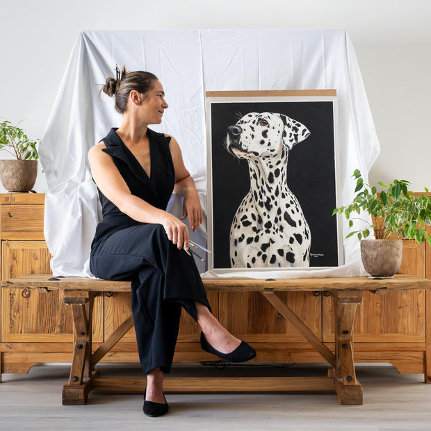 Woman sitting on a wooden bench with a framed picture of a Dalmatian dog in a room with plants.