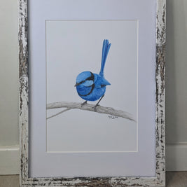 A framed drawing featuring a blue bird perched on a branch, set against a white mat and a distressed white wood frame, leaning against a light gray wall on a wood floor.