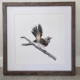 A framed bird art drawing featuring a small brown and white bird perched on a branch, set in a dark wood frame with a white mat against a neutral wall and wood floor.