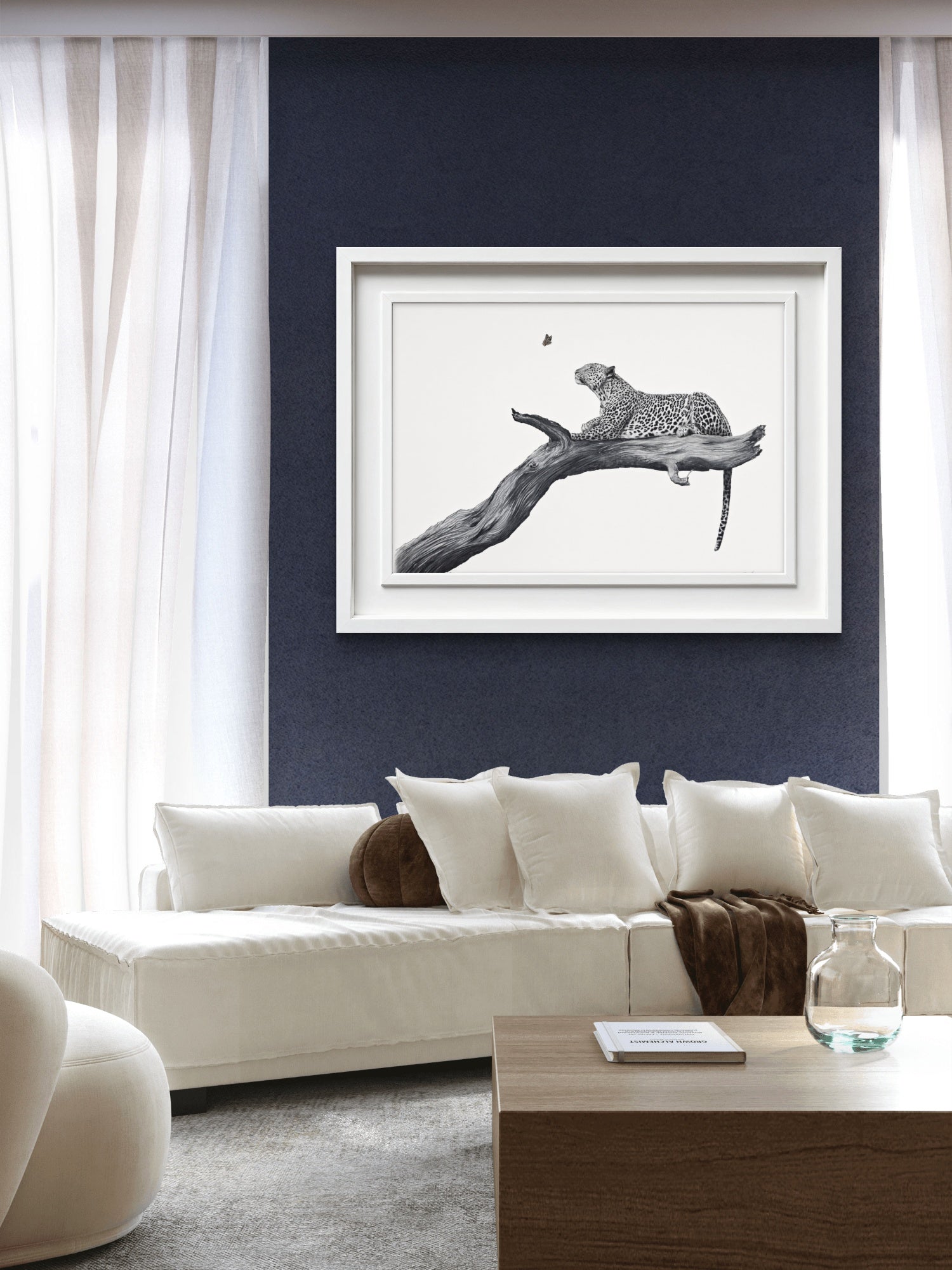 A framed black and white art print of a leopard on a branch, displayed on a dark navy blue wall above a modern white sofa in a living room setting.