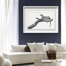 A framed black and white art print of a leopard on a branch, displayed on a dark navy blue wall above a modern white sofa in a living room setting.