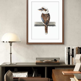 Framed artwork of a bird on a branch in a room with a desk and lamp.