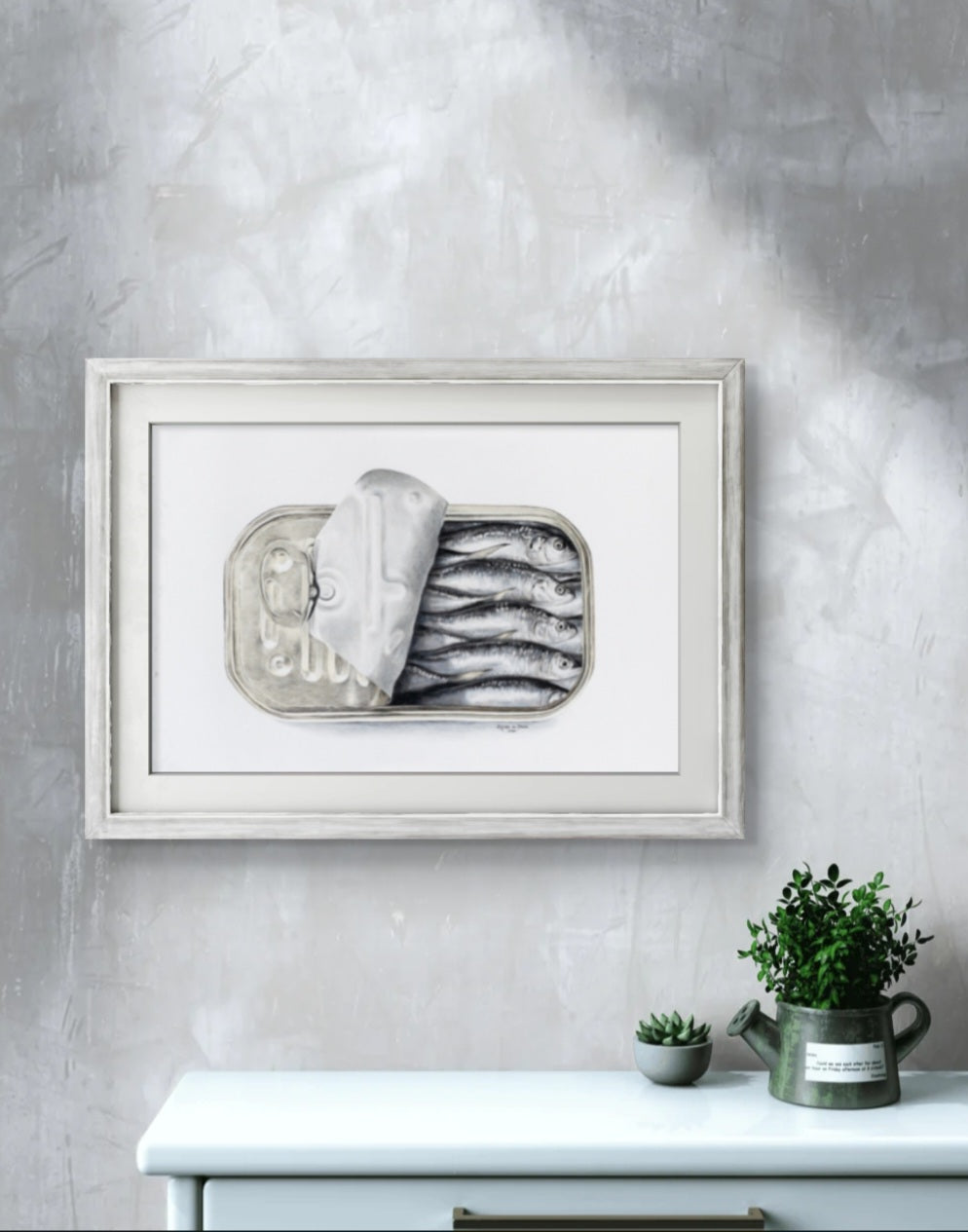 Framed artwork of a still life with fish on a gray wall above a white cabinet.