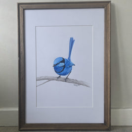 A framed drawing of a blue bird perched on a branch, set against a white mat and a rustic brown wooden frame, leaning against a neutral wall on a wood floor.