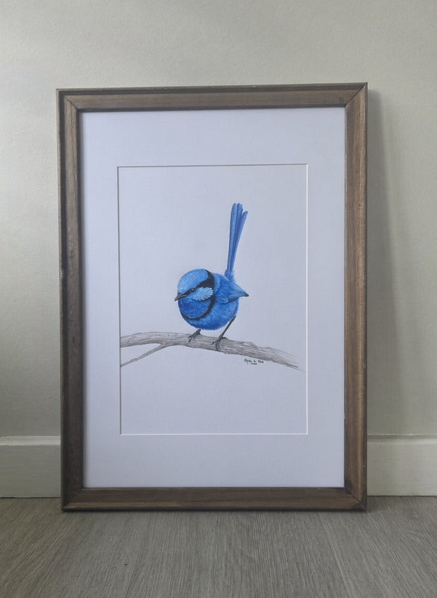A framed drawing of a blue bird perched on a branch, set against a white mat and a rustic brown wooden frame, leaning against a neutral wall on a wood floor.