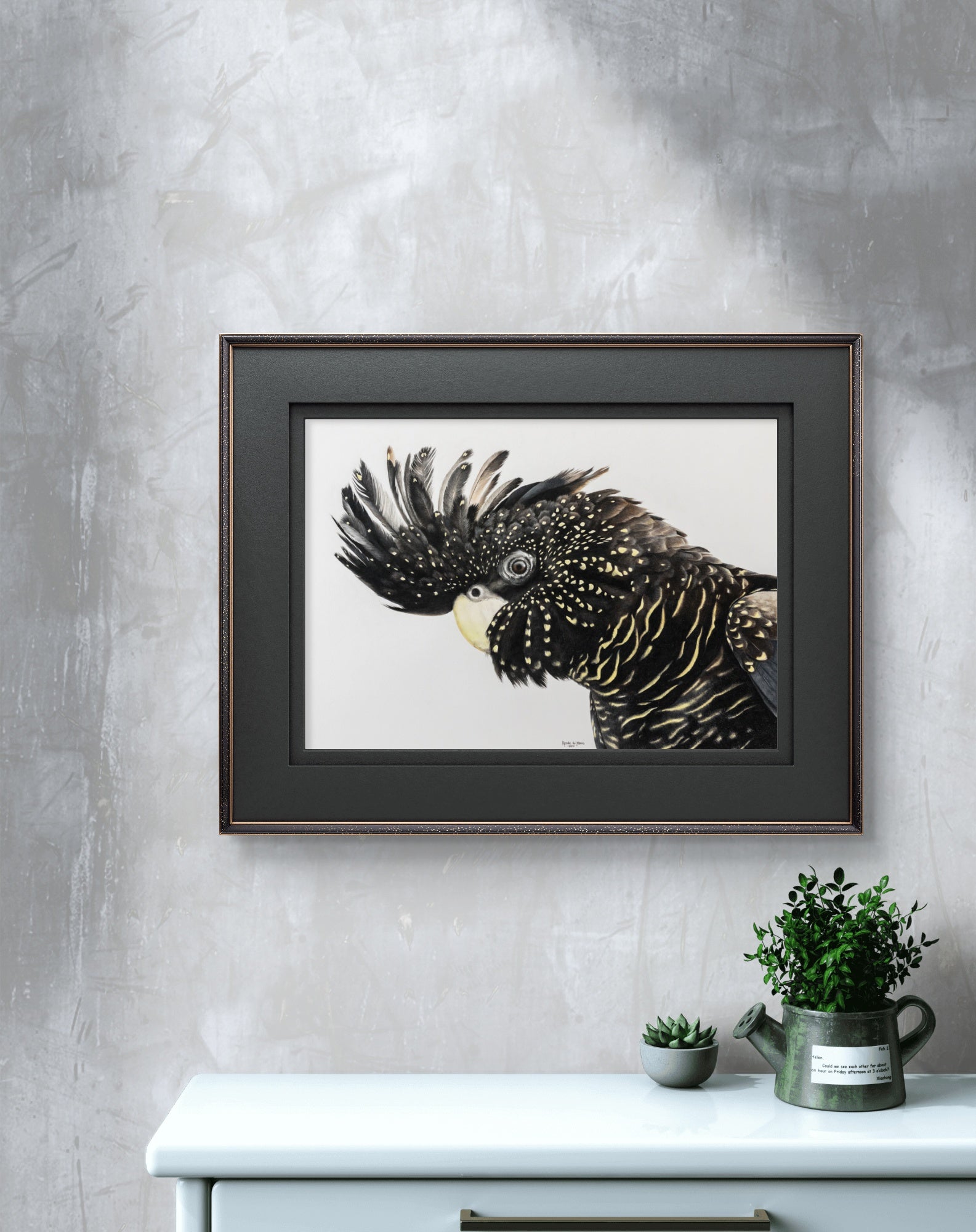 Framed artwork of a parrot on a gray wall above a white cabinet with plants.