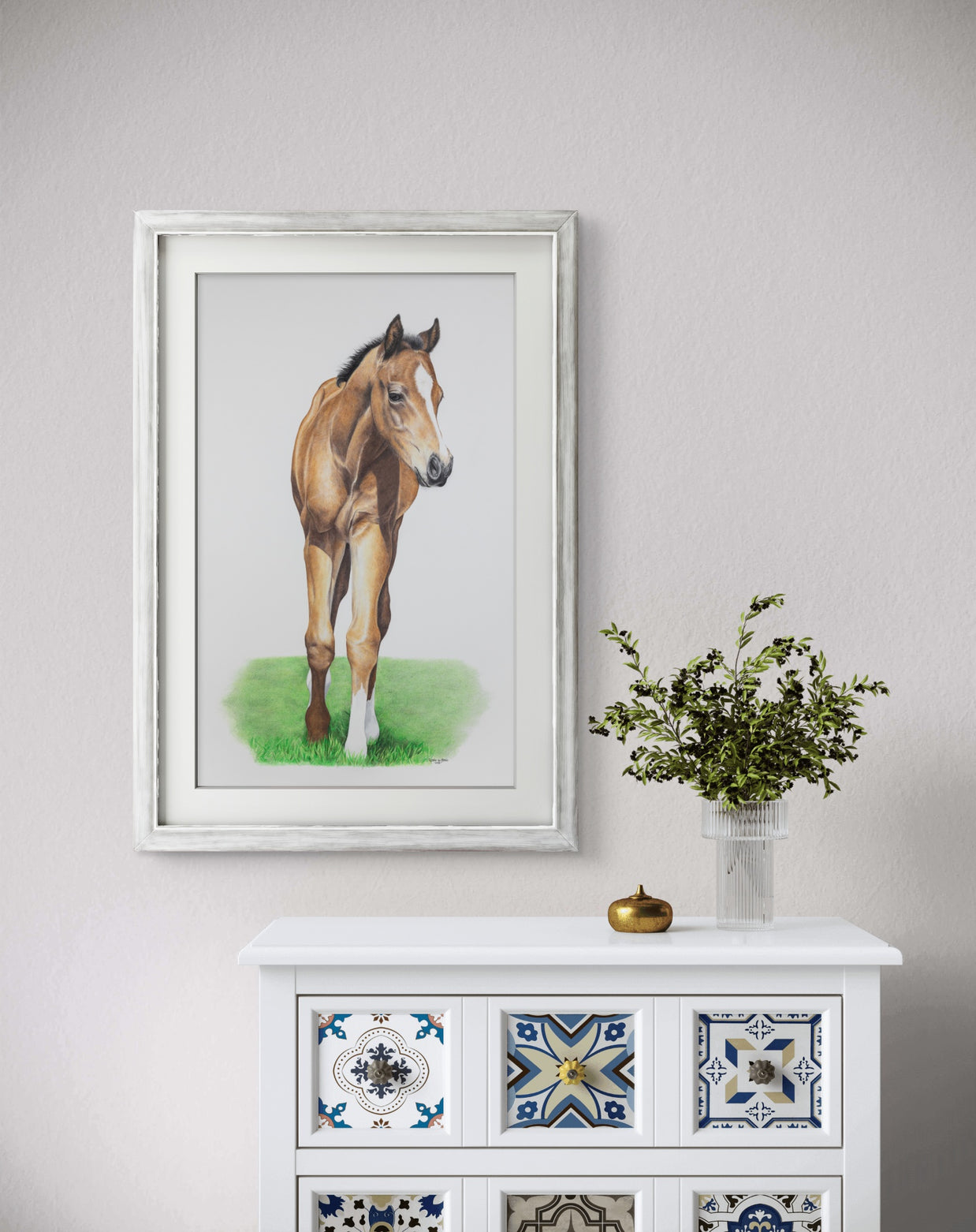 Framed painting of a horse on a wall above a decorative cabinet with a vase of flowers.