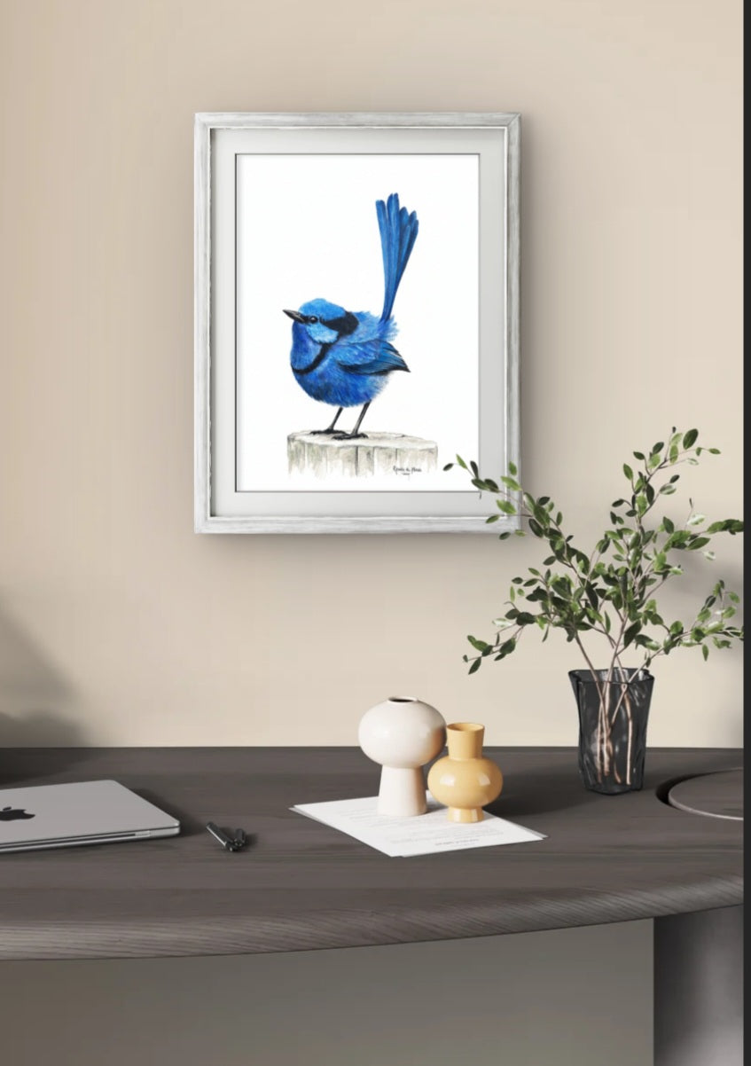 Framed artwork of a blue bird on a beige wall above a desk with decorative items.