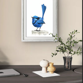 Framed artwork of a blue bird on a beige wall above a desk with decorative items.