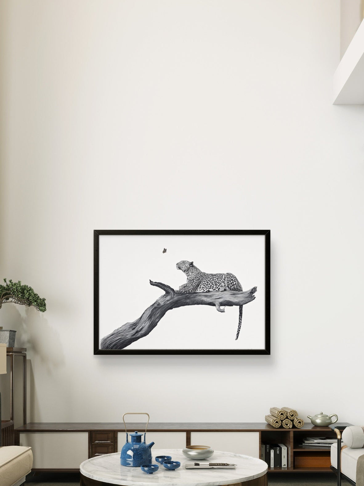 A framed black and white art print of a leopard resting on a branch, displayed on a white wall in a modern living room setting.