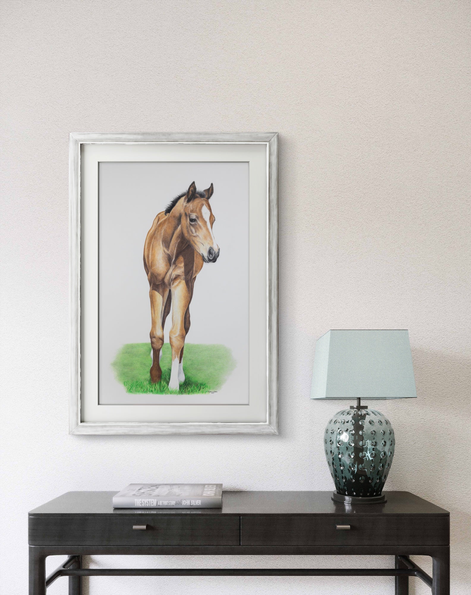 Framed picture of a horse on a wall above a table with a lamp.