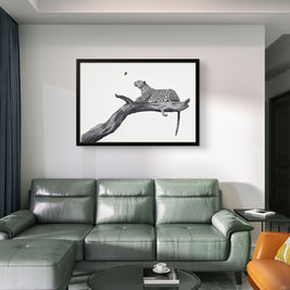 A framed black and white art print of a leopard on a branch, displayed on a white wall above a green leather sectional sofa in a modern living room setting.