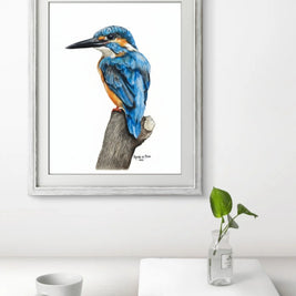 Framed artwork of a blue bird on a branch with a white mug and book on a table.