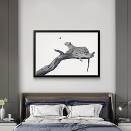 A framed black and white art print of a leopard resting on a branch, displayed on a light gray wall above a modern bed in a bedroom setting.