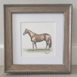A framed miniature colour pencil drawing featuring a painted brown horse, set in a white mat and a rustic brown wooden frame, resting on a light wood floor against a neutral wall.