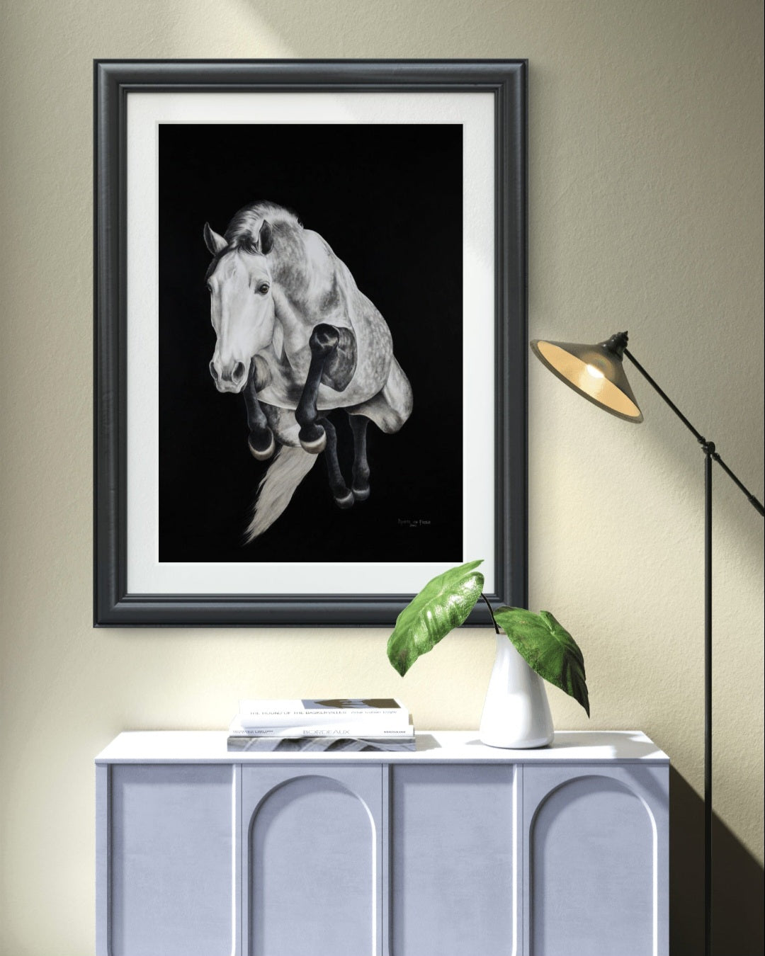 Framed artwork of a horse on a wall above a cabinet with a lamp and plant.